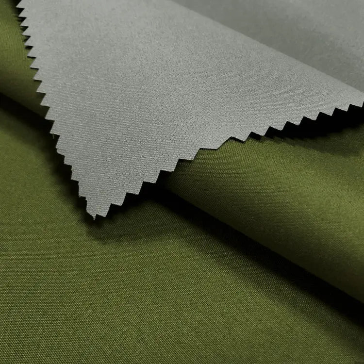 Close-up of two fabrics: gray Longan Craft Coated Waterproof Peachskin Fabric by the yard with zigzag-cut edge layered over smooth olive green rainwear material. Cozy microfiber polyester peachskin texture ideal for jackets.