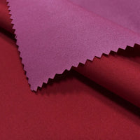 A close-up of Longan Craft's Coated Waterproof Peachskin Fabric shows a purple-pink layer with zigzag-cut edges atop smooth red microfiber polyester, both featuring a slightly shiny finish ideal for cozy jackets.