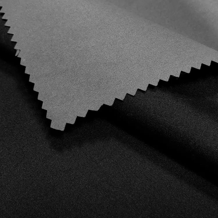 A close-up of two overlapping Longan Craft Coated Waterproof Peachskin Fabrics—one light gray, one black—both smooth and matte, expertly crafted from microfiber polyester, ideal for making cozy, waterproof jackets.