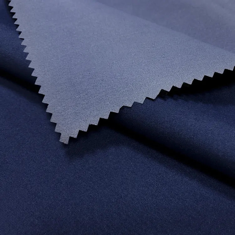 A close-up of two overlapping pieces of Longan Craft Coated Waterproof Peachskin Fabric by the Yard, featuring dark blue microfiber polyester with a zigzag-cut edge and cozy texture—ideal for jacket making and rainwear.