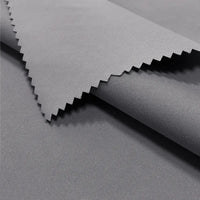 Close-up of Longan Craft Coated Waterproof Peachskin Fabric By The Yard shows smooth, gray microfiber polyester with a matte finish and pinked edge. The cozy peachskin texture is soft and ideal for rainwear or jacket making.