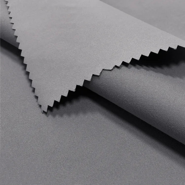 Close-up of Longan Craft Coated Waterproof Peachskin Fabric By The Yard shows smooth, gray microfiber polyester with a matte finish and pinked edge. The cozy peachskin texture is soft and ideal for rainwear or jacket making.