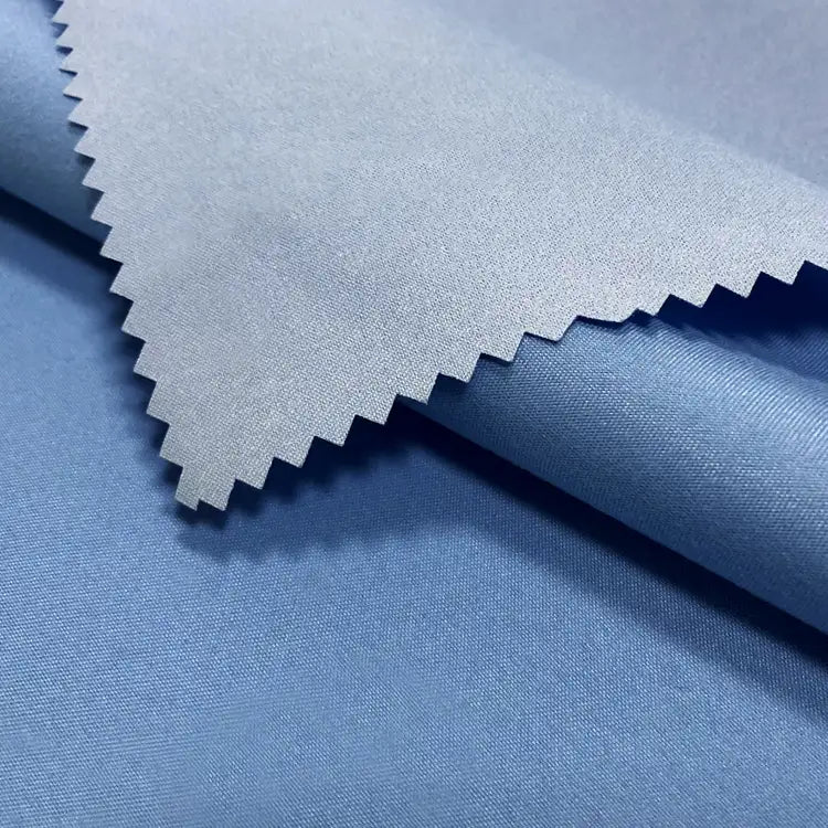 A close-up of Longan Craft's Coated Waterproof Peachskin Fabric by the Yard shows its light blue, slightly shiny microfiber polyester. The cozy peachskin texture and waterproof finish are highlighted with a zigzag-cut swatch over a rolled section.