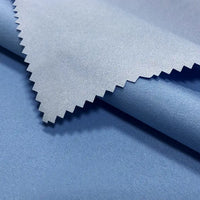 A close-up of Longan Craft's Coated Waterproof Peachskin Fabric by the Yard shows its light blue, slightly shiny microfiber polyester. The cozy peachskin texture and waterproof finish are highlighted with a zigzag-cut swatch over a rolled section.