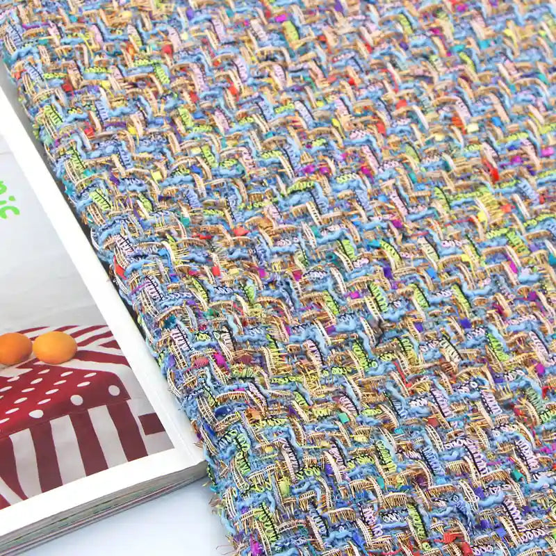 A detailed close-up of the Colorful Boucle Tweed Fabric By The Yard from Longan Craft showcases its vibrant, thick textured weave and intricate zigzag patterns, displayed next to an open magazine with a red and white polka dot design and some oranges.