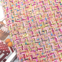 Close-up of the Colorful Boucle Tweed Fabric By The Yard from Longan Craft, featuring a thick, textured woven surface with vibrant pink, yellow, blue, and gold threads. This luxury tweed fabric for blazers is displayed atop a magazine with an image of a basket and polka-dotted cloth.