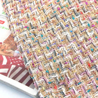 Close-up of the Longan Craft Colorful Boucle Tweed Fabric By The Yard, featuring thick, textured weaving with vibrant gold, pink, blue, and white threads. This luxury tweed material for blazers is displayed atop magazines—one showing a red and white striped cover with a wicker basket image.