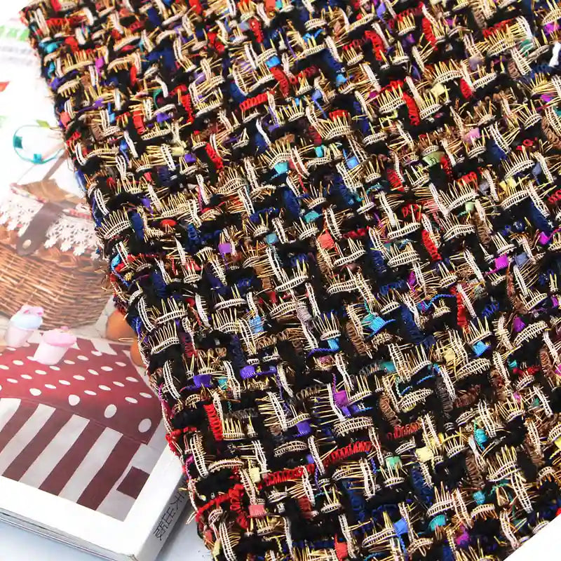 A close-up of Longan Craft’s Colorful Boucle Tweed Fabric By The Yard showcases the thick, luxury woven texture, with interwoven threads in brown, gold, red, blue, and black capturing the intricate details of this premium material for blazers. The fabric is displayed atop a partially visible magazine featuring a cake photograph.