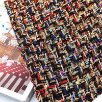 A close-up of Longan Craft’s Colorful Boucle Tweed Fabric By The Yard showcases the thick, luxury woven texture, with interwoven threads in brown, gold, red, blue, and black capturing the intricate details of this premium material for blazers. The fabric is displayed atop a partially visible magazine featuring a cake photograph.