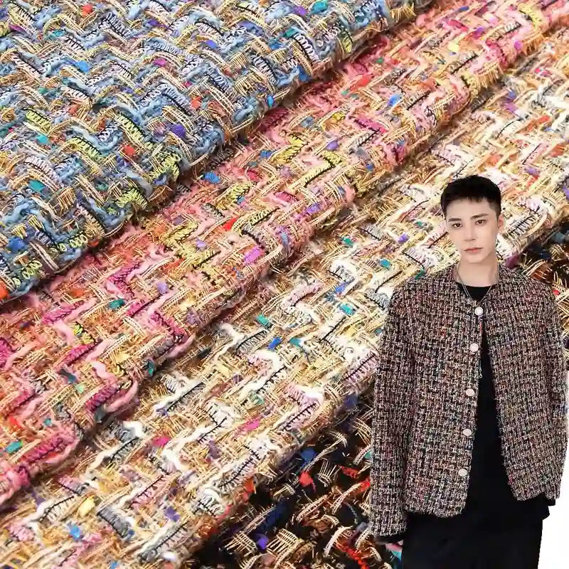 A person wearing a jacket crafted from Longan Craft’s Colorful Boucle Tweed Fabric By The Yard—a thick, textured woven tweed material—stands in front of stacked rolls of the luxury tweed fabric for blazers in various bright hues.