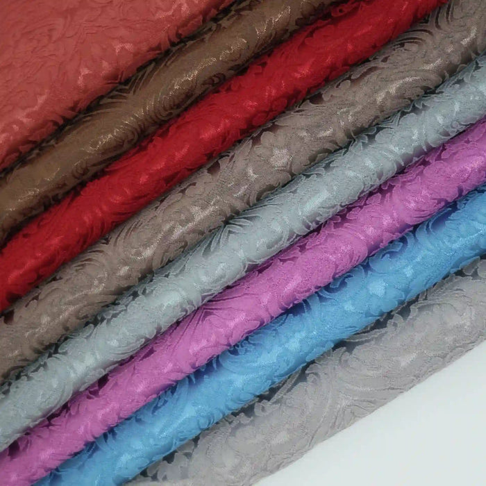 A stack of Longan Craft's Colorful Brocade Damask Fabric by the yard, each with intricate raised florals in brown, red, gray, blue, and purple—ideal as patterned jacquard damask dress material or for upholstery projects.