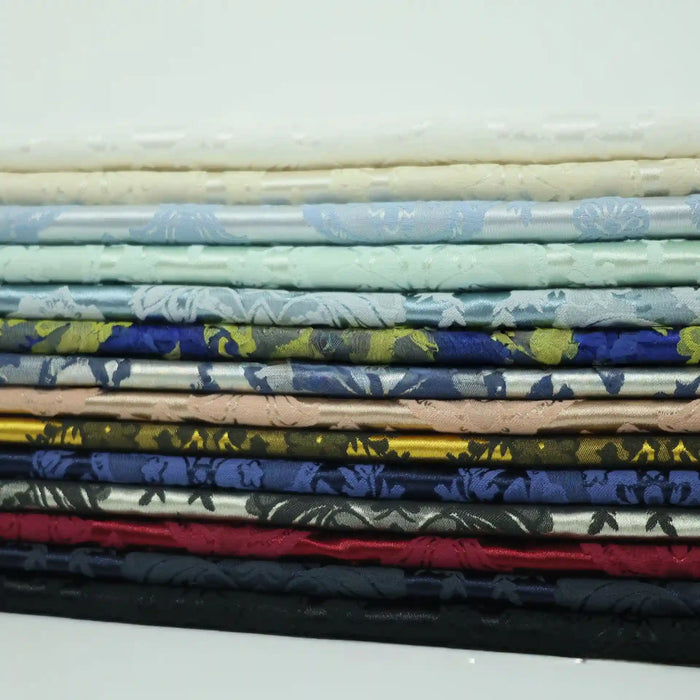 A stack of vibrant Longan Craft Colorful Cotton Damask Fabrics in white, blue, gold, red, and black is neatly arranged to showcase the antique floral damask weave—ideal for upholstery or decor by the yard.