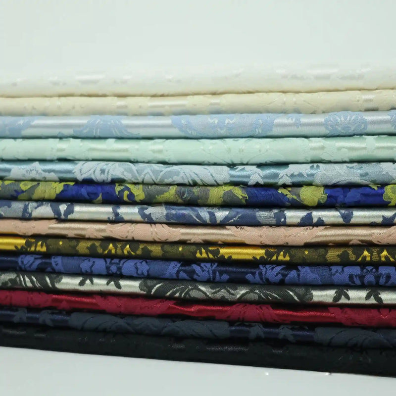 A stack of vibrant Longan Craft Colorful Cotton Damask Fabrics in white, blue, gold, red, and black is neatly arranged to showcase the antique floral damask weave—ideal for upholstery or decor by the yard.