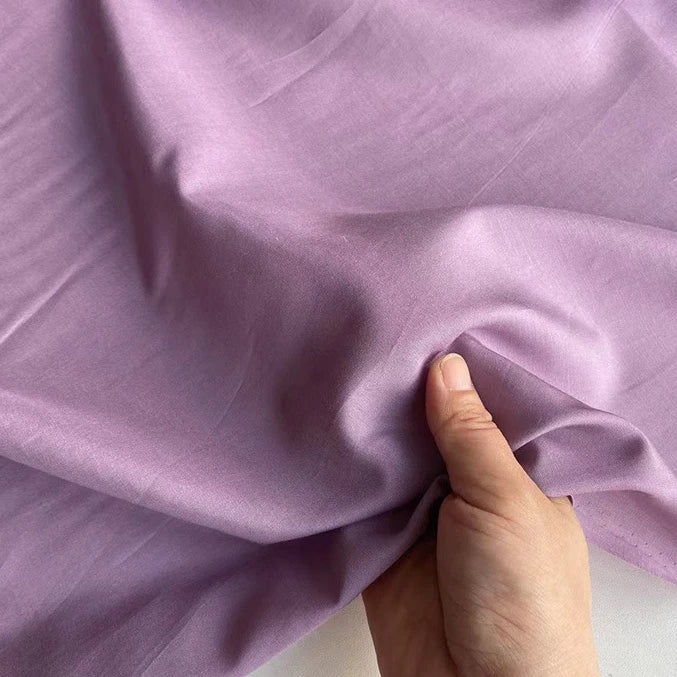 A hand pinches and lifts a soft, smooth piece of Longan Craft's Colorful Cotton Silk Fabric By The Yard—lightweight mulberry silk material—showcasing elegant folds in this breathable silk lining fabric.
