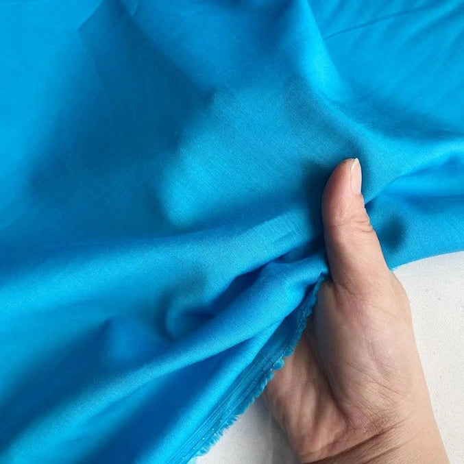 A hand displays Longan Craft’s Colorful Cotton Silk Fabric By The Yard—lightweight, breathable Mulberry silk—against a white background, emphasizing its smooth texture and gently frayed edge.