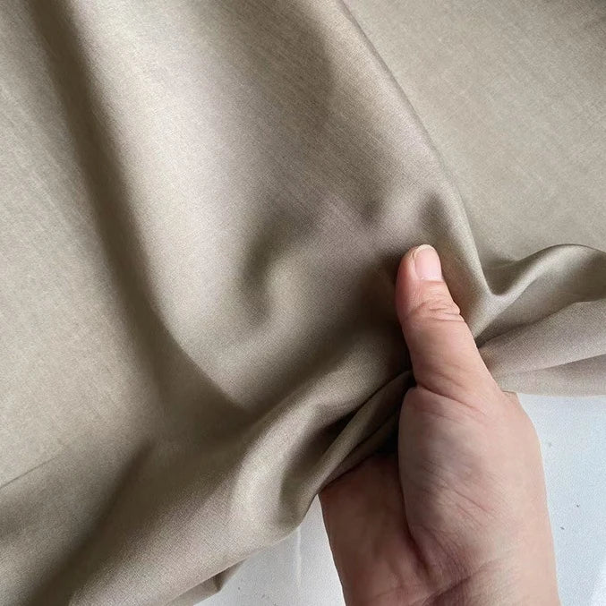 A hand gently lifts Longan Craft’s Colorful Cotton Silk Fabric By The Yard, revealing its soft, smooth, light beige surface—showcasing the lightweight, breathable mulberry silk material perfect for lining.