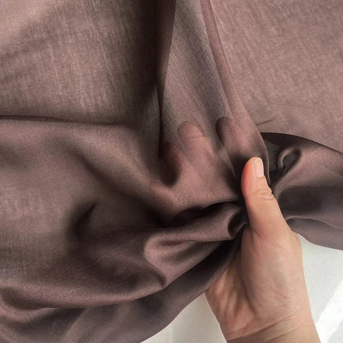 A hand gently holds a piece of Longan Craft’s Colorful Cotton Silk Fabric By The Yard, lightweight mulberry silk material, creating soft folds and shadows in this premium, breathable silk lining fabric.