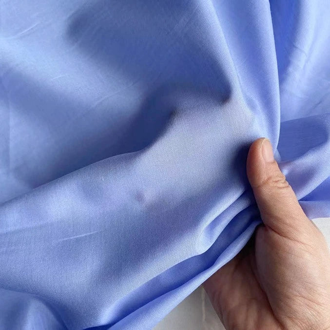 A hand gently holds Longan Craft's Colorful Cotton Silk Fabric By The Yard, a lightweight, breathable mulberry silk material that highlights its smooth texture and soft appearance.