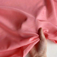 A hand gently holds and gathers Longan Craft's Colorful Cotton Silk Fabric by the yard—a lightweight, breathable Mulberry silk lining fabric in soft light pink.
