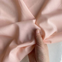 A hand gently gathers Longan Craft’s Colorful Cotton Silk Fabric, a light pink, lightweight mulberry silk material, creating soft folds in this breathable silk lining fabric by the yard.