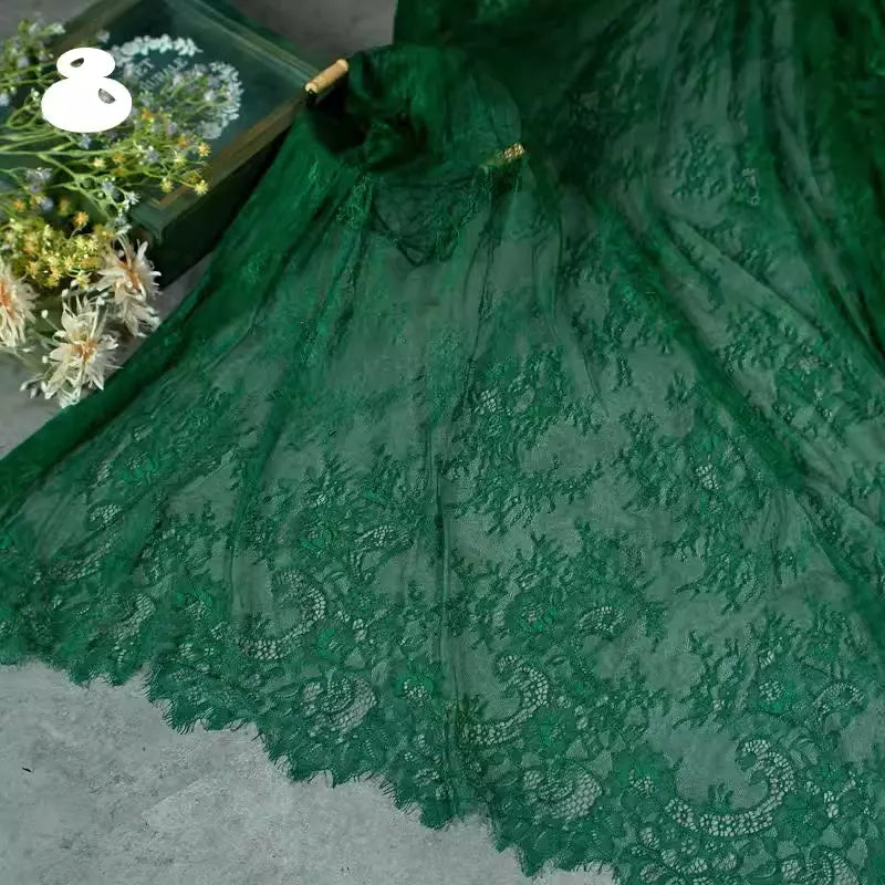 A close-up of Longan Craft’s Colorful Floral Embroidered Lace Fabric By The Yard, featuring vintage scalloped edges and botanical patterns, is displayed on gray beside a box of assorted white and yellow flowers.