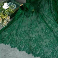 A close-up of Longan Craft’s Colorful Floral Embroidered Lace Fabric By The Yard, featuring vintage scalloped edges and botanical patterns, is displayed on gray beside a box of assorted white and yellow flowers.