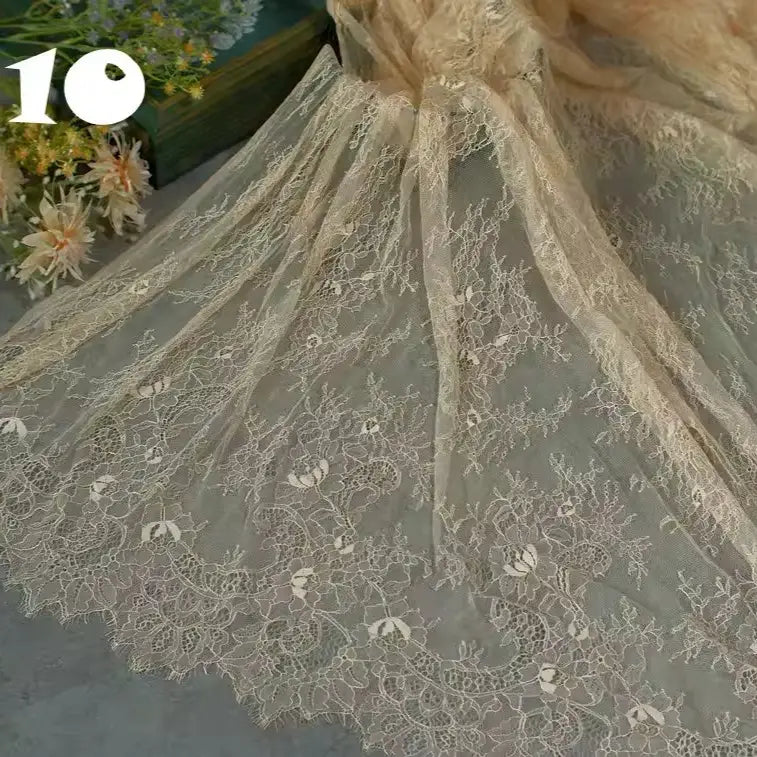 Colorful Floral Embroidered Lace Fabric by Longan Craft, featuring vintage scalloped edges and a botanical pattern, lies flat beside pale flowers; ideal for wedding gowns. The number 10 is shown in the top left corner.