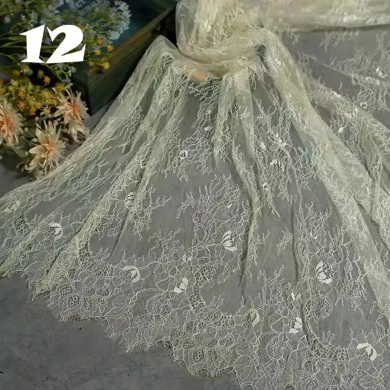 Longan Craft’s Colorful Floral Embroidered Lace Fabric By The Yard, featuring a vintage scalloped botanical pattern, is delicately spread out for display. Flowers and greenery appear in the background with the number 12 on the top left.