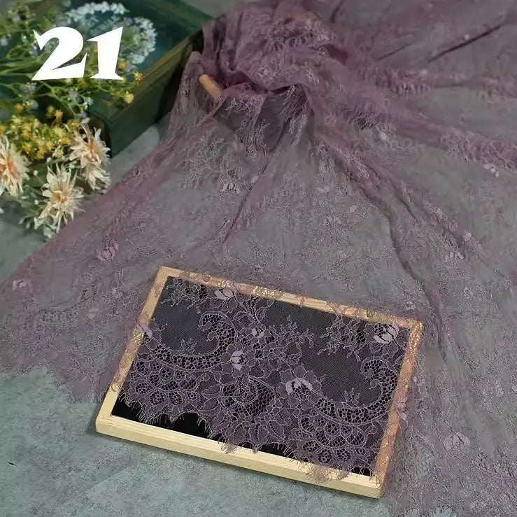 Longan Craft’s Colorful Floral Embroidered Lace Fabric by the yard features vintage scalloped edges and botanical designs in purple, elegantly draped with a wooden frame, ideal for wedding gowns or evening wear. A white bouquet and “21” accent the scene.