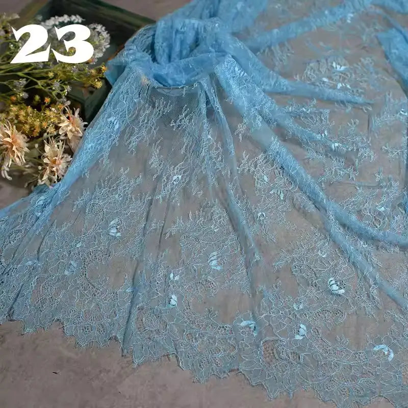 Longan Craft’s Colorful Floral Embroidered Lace Fabric by the Yard, featuring vintage scalloped edges and a botanical pattern, is displayed with intricate sheer detail—ideal for delicate wedding gowns. A bouquet and bold white “23” appear in the background.