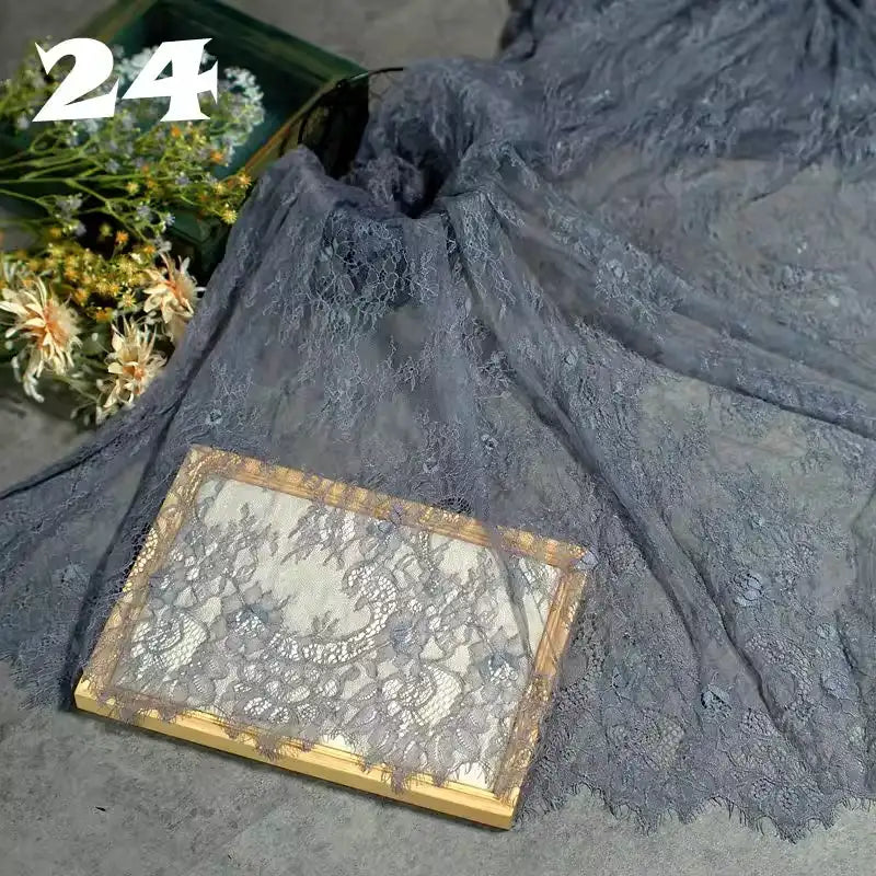 A piece of Longan Craft Colorful Floral Embroidered Lace Fabric By The Yard with a vintage botanical pattern is draped over a surface, partially covering flowers and a book. The number 24 appears in the top left corner.