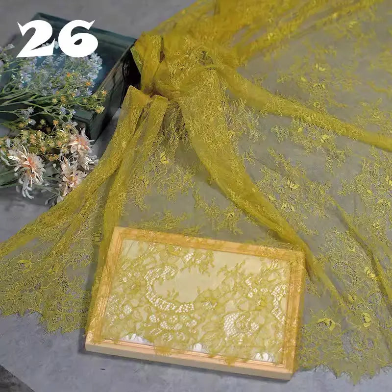 Colorful Floral Embroidered Lace Fabric by Longan Craft is displayed across a gray surface, with a box wrapped in the same botanical-patterned lace. White and green flowers sit on the left, and "26" appears at the top left.