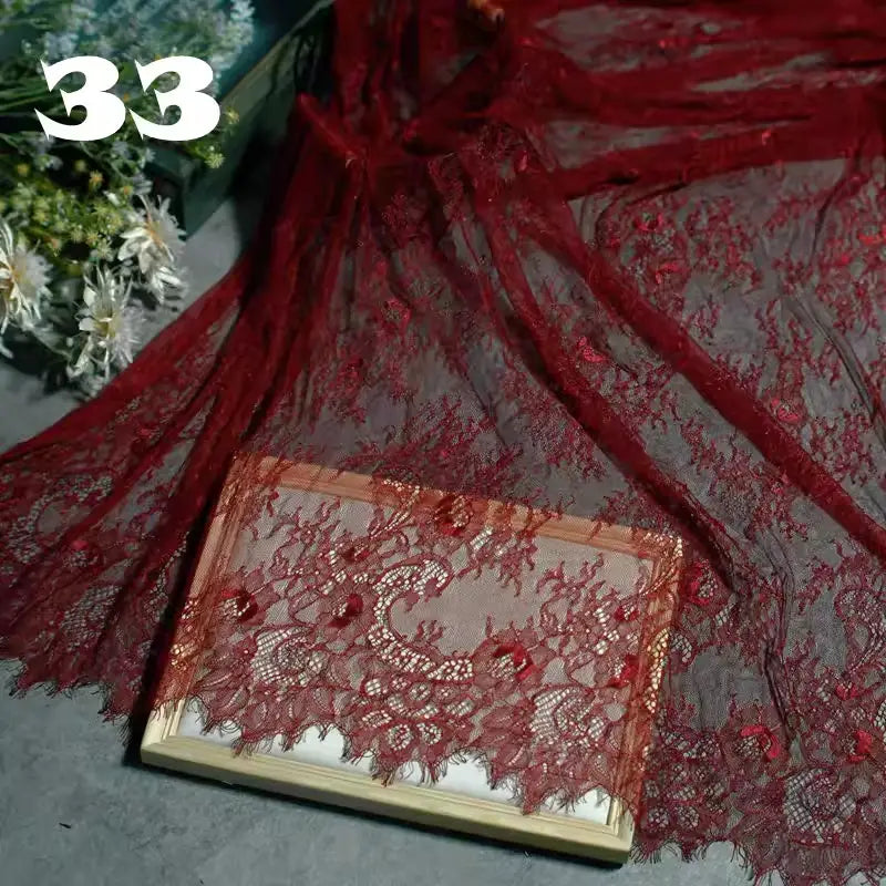 Colorful Floral Embroidered Lace Fabric by Longan Craft, numbered 33, draped over a book. This vintage scalloped botanical lace features semi-sheer detailing with green and white floral accents softly visible in the background.