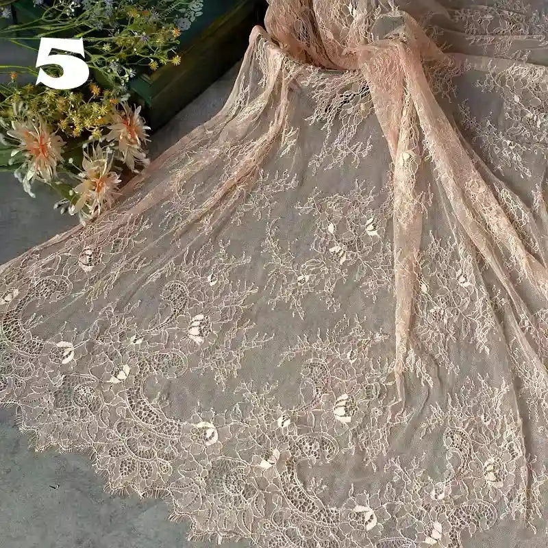 A yard of Longan Craft's Colorful Floral Embroidered Lace Fabric with vintage scalloped edge and botanical pattern is displayed on a gray surface, ideal for wedding gowns. Artificial flowers and a white number 5 are in the upper left corner.