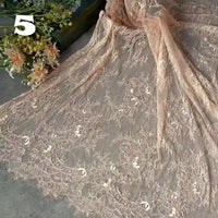 A yard of Longan Craft's Colorful Floral Embroidered Lace Fabric with vintage scalloped edge and botanical pattern is displayed on a gray surface, ideal for wedding gowns. Artificial flowers and a white number 5 are in the upper left corner.