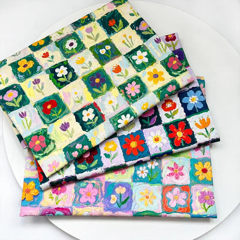 Three folded pieces of Colorful Floral Print Canvas Fabric By The Yard featuring a colorful floral print with a grid pattern of hand-painted style flowers.