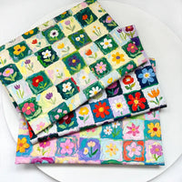 Three folded pieces of Colorful Floral Print Canvas Fabric By The Yard featuring a colorful floral print with a grid pattern of hand-painted style flowers.