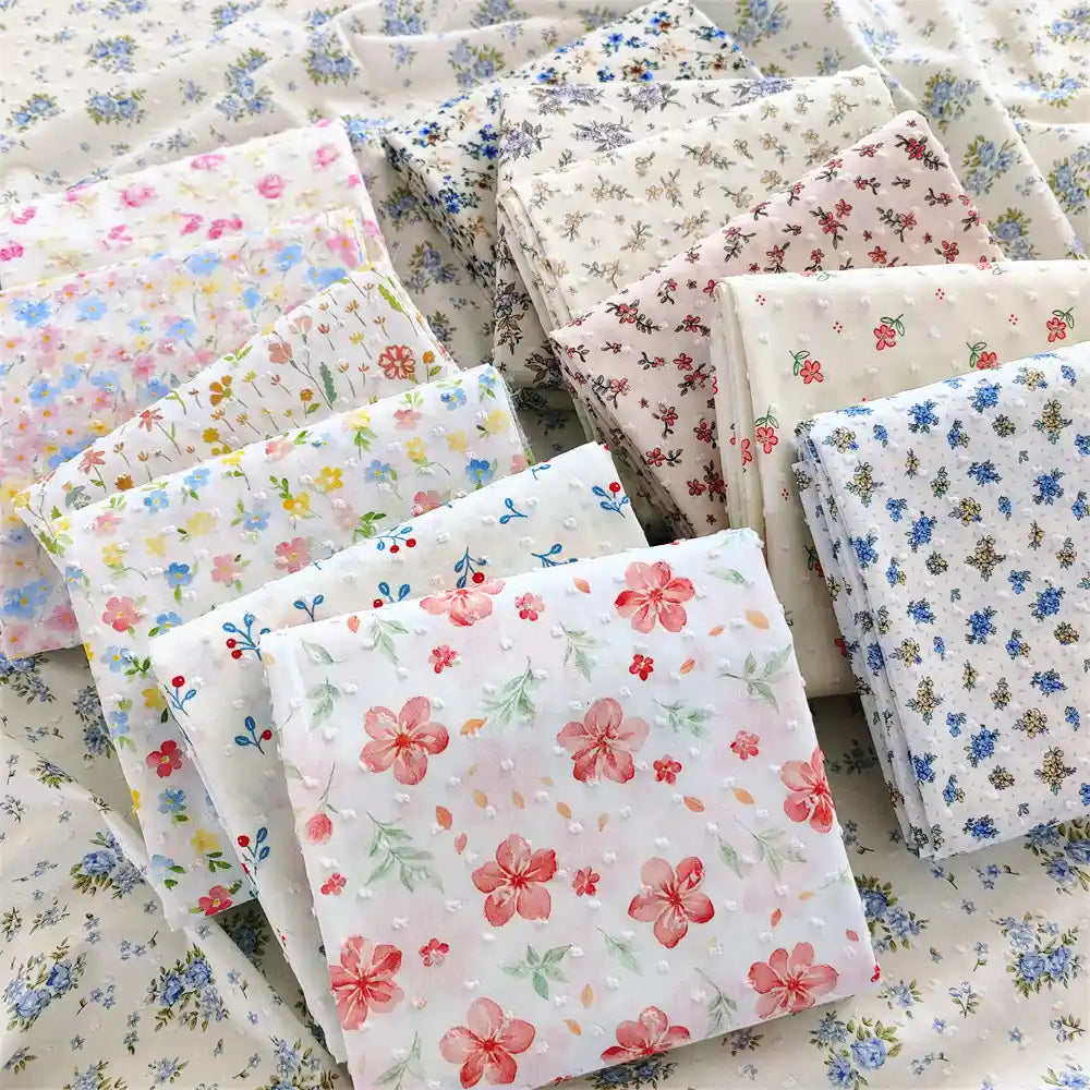Several stacks of Longan Craft's Colorful Flower Printed Swiss Dot Fabric By The Yard, made from breathable cotton with vibrant floral patterns, are displayed on a surface covered in matching dotted swiss material—perfect for loungewear projects.