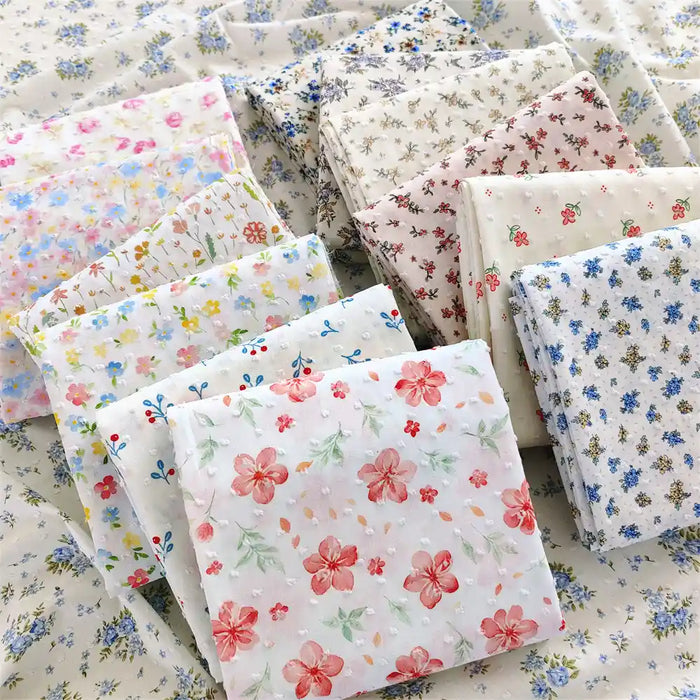 Several stacks of Longan Craft's Colorful Flower Printed Swiss Dot Fabric By The Yard, made from breathable cotton with vibrant floral patterns, are displayed on a surface covered in matching dotted swiss material—perfect for loungewear projects.