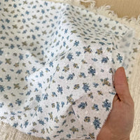 A hand holds Longan Craft’s Colorful Flower Printed Swiss Dot Fabric by the yard—breathable cotton with a blue and yellow floral pattern, frayed edges, and soft texture, perfect for loungewear.