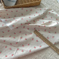 Longan Craft’s Colorful Flower Printed Swiss Dot Fabric by the yard, a cotton material with floral pattern, is spread on a textured surface with a wooden ruler and woven basket nearby. A blue object with text appears in the corner.