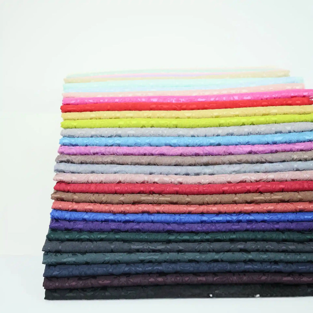 A stack of Longan Craft’s Colorful Jacquard Damask Fabric By The Yard showcases floral patterns from light to dark shades, making vibrant upholstery fabric that stands out against a white background.