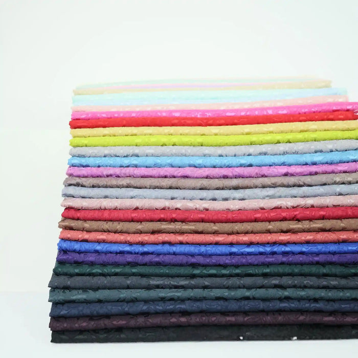 A stack of Longan Craft’s Colorful Jacquard Damask Fabric By The Yard showcases floral patterns from light to dark shades, making vibrant upholstery fabric that stands out against a white background.