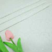 A light pink artificial tulip with green leaves rests on neatly folded Colorful Jacquard Damask Fabric By The Yard from Longan Craft, a floral patterned upholstery textile shown in white in the background.