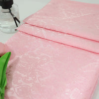 A folded piece of Colorful Jacquard Damask Fabric By The Yard from Longan Craft, featuring a floral pattern, lies on a white surface beside a green artificial flower and a clear spray bottle.