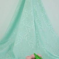 Longan Craft’s Colorful Jacquard Damask Fabric By The Yard, featuring an elegant floral pattern, is gracefully draped with pink artificial flowers and green leaves adding charm to this stylish home décor upholstery display.