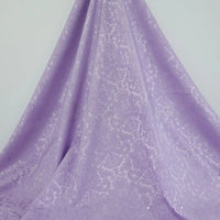 A light purple Longan Craft Colorful Jacquard Damask Fabric By The Yard featuring a subtle floral pattern is elegantly draped against a plain background—ideal as damask jacquard upholstery fabric for sophisticated home décor.