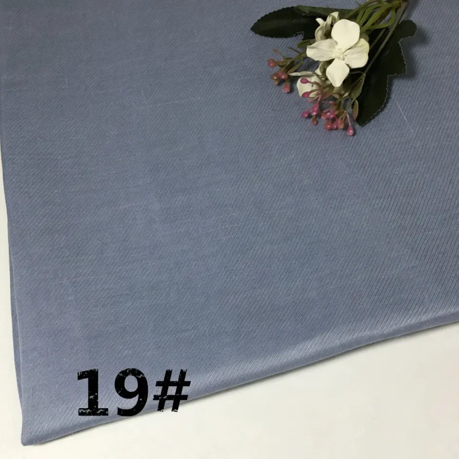 A folded piece of light blue Longan Craft Colorful Lightweight Ramie Fabric by the yard rests on a white surface, marked with the number 19# in black, while artificial flowers decorate one corner.