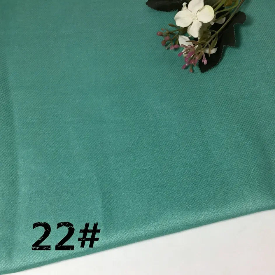 A soft, teal-colored Longan Craft Colorful Lightweight Ramie Fabric By The Yard features the number 22# printed in black in the lower left corner. A small bouquet of artificial white and purple flowers rests in the upper right, emphasizing this pure ramie material’s breathable versatility and charm for garment making.