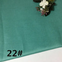A soft, teal-colored Longan Craft Colorful Lightweight Ramie Fabric By The Yard features the number 22# printed in black in the lower left corner. A small bouquet of artificial white and purple flowers rests in the upper right, emphasizing this pure ramie material’s breathable versatility and charm for garment making.